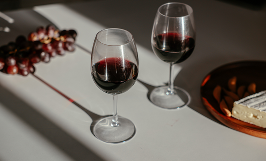 two glasses of red wine next to plate of grapes and cheese