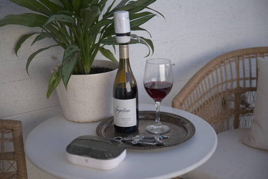 Aervana Travel wine aerator on a red wine bottle next to a glass of red wine and the Aervana Travel carrying case