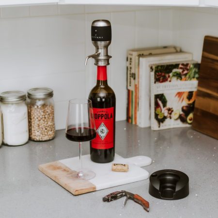 Original Wine Aerator on wine bottle next to filled wine glass and branded corkscrew in a kitchen with cookbooks in the background