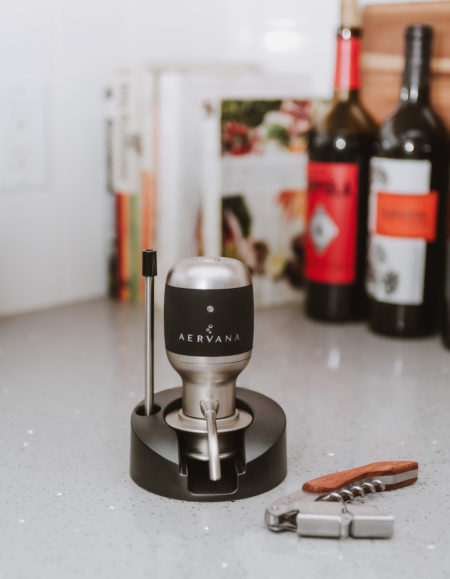 Original Wine Aerator in its stand next to branded corkscrew with wine bottles and cookbooks in background